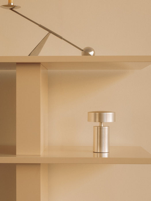Brushed aluminium Column Table Lamp, Portable on a beige shelf below an Interconnect Candle Holder in a minimalist setting.