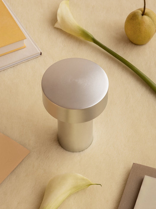 Overhead view of the Column Table Lamp in brushed aluminium on a cream rug surrounded by books, calla lilies, and a pear.