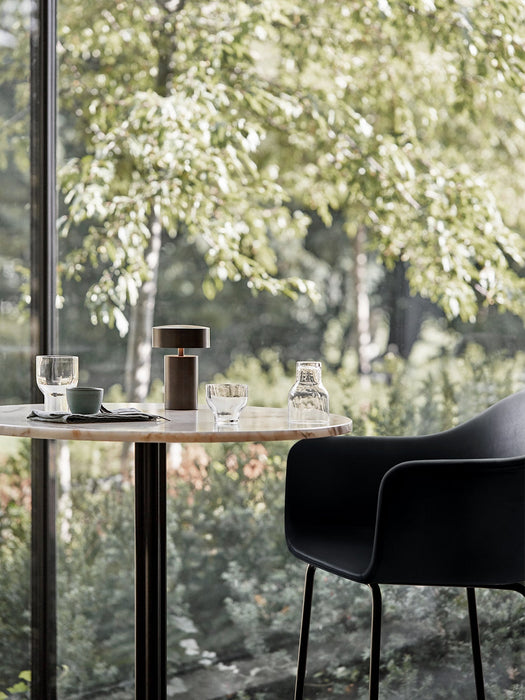 A Column Table Lamp on a marble cafe table, next to a black Harbour Bar Chair. The table is by a window with a garden view.