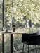 A Column Table Lamp on a marble cafe table, next to a black Harbour Bar Chair. The table is by a window with a garden view.