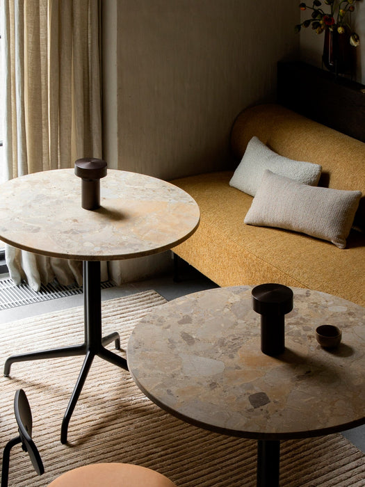 Lounge setting with two marble-topped tables, each displaying a bronze portable Column Table Lamp, next to a yellow sofa.