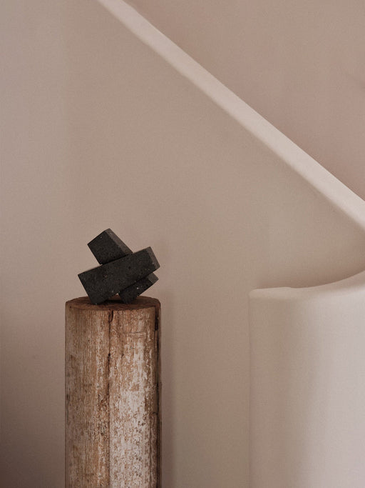 A pair of dark, textured Converge Book Ends styled as a sculpture on a weathered log against a soft, neutral wall.