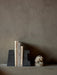 A pair of black, textured Converge Book Ends holding four books upright on a shelf, next to a small, pale abstract sculpture.