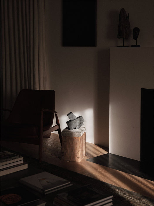 The sculptural, dark grey Converge Book Ends sit on a wooden pedestal, illuminated by a sunbeam in a dimly lit, elegant room.