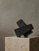 The black, porous Converge Book End, formed of three interlocking blocks, sits sculpturally atop a beige marble plinth.