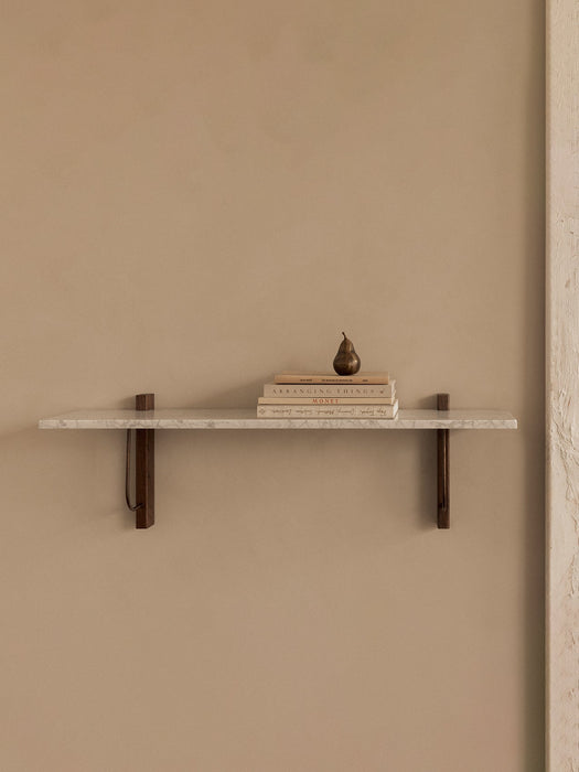Front view of the long Corbel Shelf with a white marble top and dark wood brackets. It is styled with books and a pear.