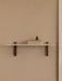 Front view of the long Corbel Shelf with a white marble top and dark wood brackets. It is styled with books and a pear.