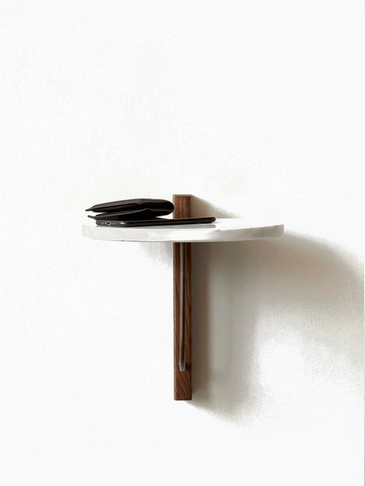 A wall-mounted Corbel Shelf with a round white marble top and a dark wood bracket, holding a black wallet and smartphone.