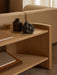 Close-up of the light oak Crescent Shelving H60 styled with vases and books, next to the corner of a beige Eave Modular Sofa.
