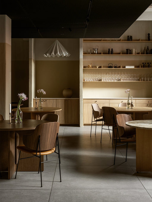 The white Dancing Pendant Lamp hangs in a softly lit restaurant, surrounded by wooden dining tables and chairs.