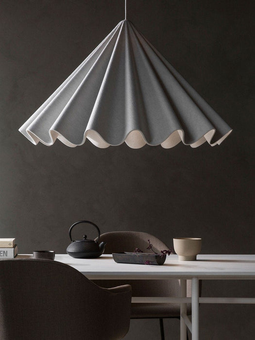 The grey, pleated Dancing Pendant Lamp illuminates a dining setting with Harbour Chairs, a black teapot, and a Split Tray.