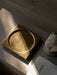 The square brass Divot Tray sits on a textured grey surface, illuminated by a sliver of sunlight next to a stone sculpture.