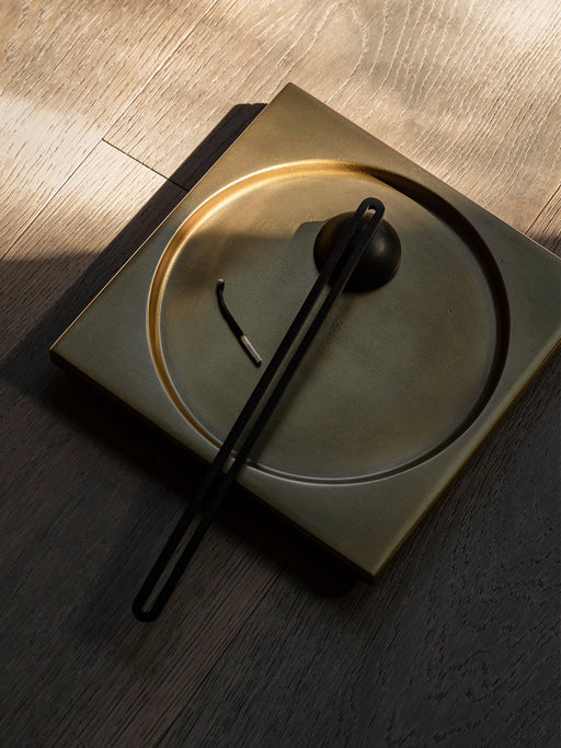 Close-up, overhead shot of the brass Divot Tray on a dark wood floor. Sunlight highlights the tray holding a burnt match.