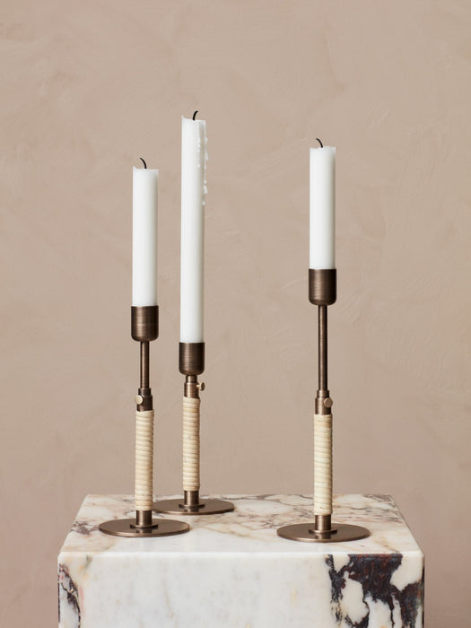 A trio of Duca Candlesticks, featuring adjustable bronzed brass stems wrapped in rattan, displayed on a veined marble block.