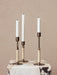 A trio of Duca Candlesticks, featuring adjustable bronzed brass stems wrapped in rattan, displayed on a veined marble block.