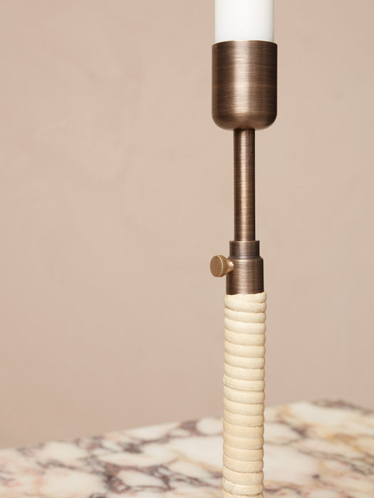 Close-up of Duca candlestick in bronzed brass, showing the rattan-wrapped handle and adjustment screw on a marble surface.