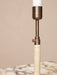 Close-up of Duca candlestick in bronzed brass, showing the rattan-wrapped handle and adjustment screw on a marble surface.