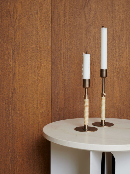 Two Duca Candleholders with white candles on a cream marble Androgyne Side Table, set against a dark wood-panelled wall.