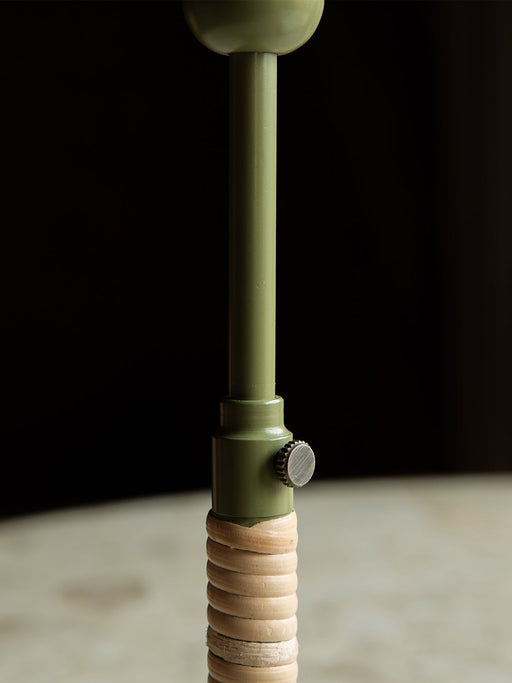 Close-up shot of the Duca Candle Holder, focusing on its olive green stem, brass adjustment knob, and rattan-wrapped base.
