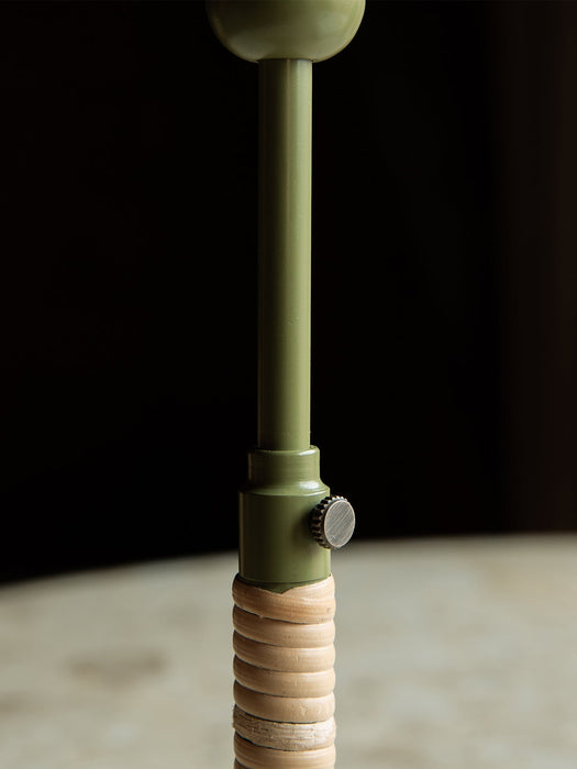 Close-up shot of the Duca Candle Holder, focusing on its olive green stem, brass adjustment knob, and rattan-wrapped base.