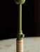 Close-up shot of the Duca Candle Holder, focusing on its olive green stem, brass adjustment knob, and rattan-wrapped base.