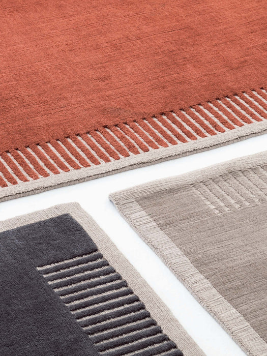 A detailed close-up of the Duomo Rug in three colours—terracotta, charcoal and beige—showing the textured striped border.