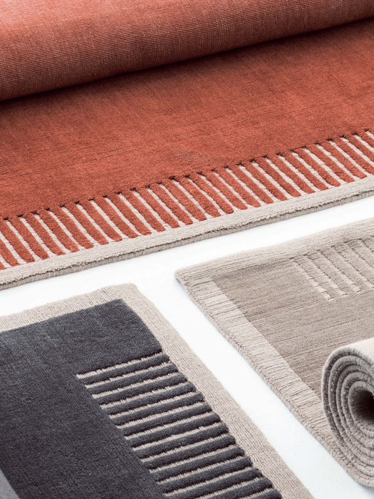 A close-up of the Duomo Rug in three colourways: rust orange, dark grey, and beige highlighting their woven texture.