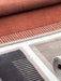 A close-up of the Duomo Rug in three colourways: rust orange, dark grey, and beige highlighting their woven texture.