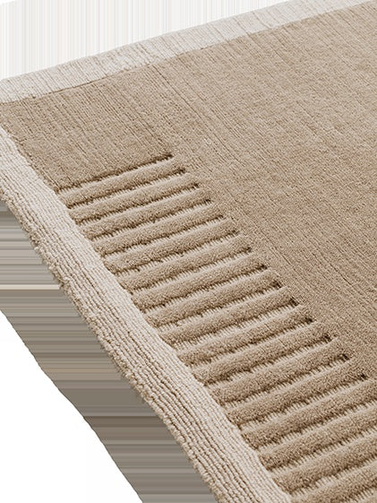 A detailed corner view of the Duomo Rug in Limestone Beige, showing its soft pile, woven border, and raised ribbed pattern.
