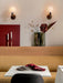 A mustard Eave Dining Sofa at a marble table set with a plate and red napkin. Behind, a ledge holds a vase and candles.