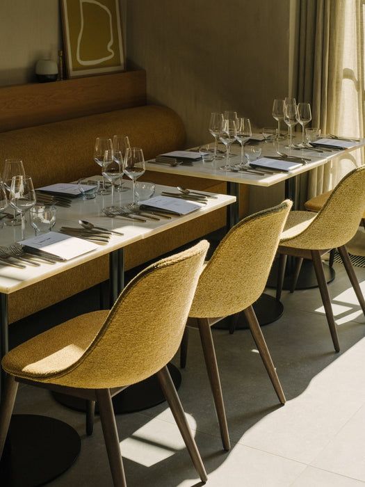 A row of yellow Harbour Dining Side Chairs beside marble-topped Harbour Column Tables, with a matching Eave Dining Sofa.
