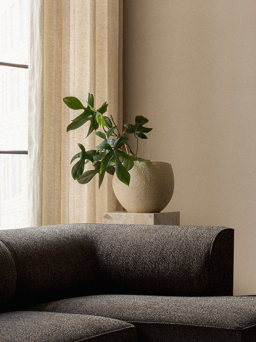 A close-up of the corner of a dark, textured Eave Modular Sofa. Behind it, a beige Plantas Planter with a green plant sits.