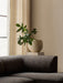 A close-up of the corner of a dark, textured Eave Modular Sofa. Behind it, a beige Plantas Planter with a green plant sits.