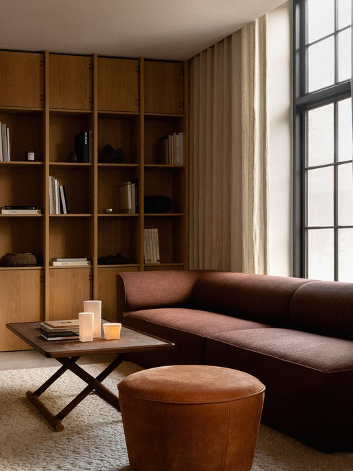 The Eave Modular Sofa in rust brown sits beside a Jager Lounge Table and a leather pouf in a warmly lit living room setting.
