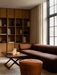 The Eave Modular Sofa in rust brown sits beside a Jager Lounge Table and a leather pouf in a warmly lit living room setting.