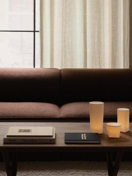 Three glowing Ignus Flameless Candles and books on a dark wood Jager Lounge Table in front of a brown Eave Modular Sofa.