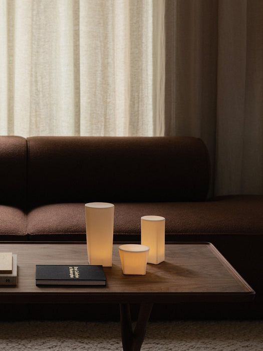 A dark wood Jager Lounge Table with three lit Ignus Flameless Candles, styled in front of a brown Eave Modular Sofa.