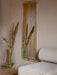 A beige Eave Modular Sofa next to an Echasse Vase with dried flowers. On the wall behind hangs a brass-framed Nimbus Mirror.