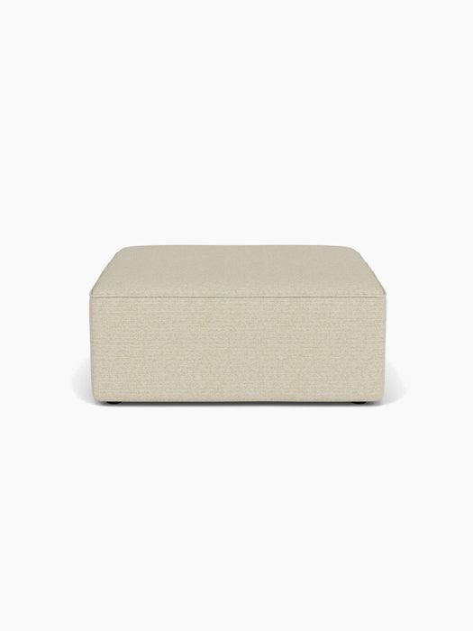 A front-on view of the Eave Modular Sofa, 96, Pouf, a rectangular pouf upholstered in a light beige textured fabric.