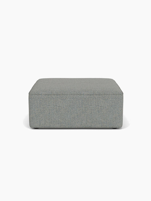 Front view of the Eave Modular Sofa, 96, Pouf, a square ottoman upholstered in textured, greyish-blue Safire 012 fabric.