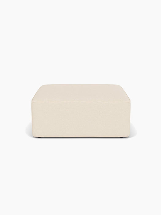 Front view of the Eave Modular Sofa, 96, Pouf. The rectangular pouf is upholstered in a light cream Logan Jasmine fabric.