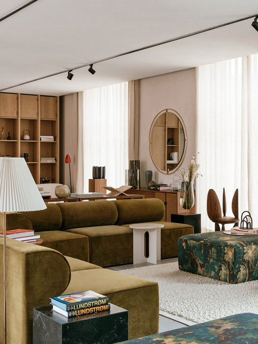 An olive green Eave Modular Sofa in a bright, modern living room with wooden furniture, a patterned ottoman, and a white rug.