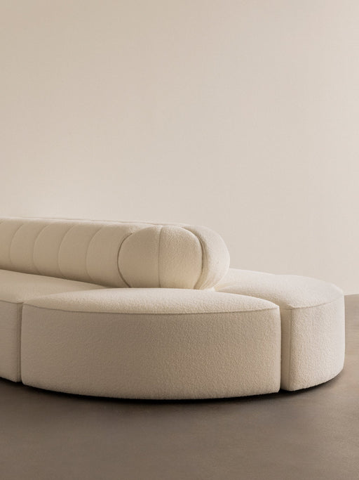 A close-up of the Eave Seamline Modular Sofa corner piece showcasing its curved form and textured, cream-coloured upholstery.