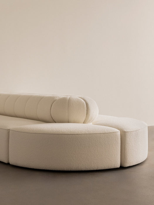 A close-up of the Eave Seamline Modular Sofa corner piece showcasing its curved form and textured, cream-coloured upholstery.