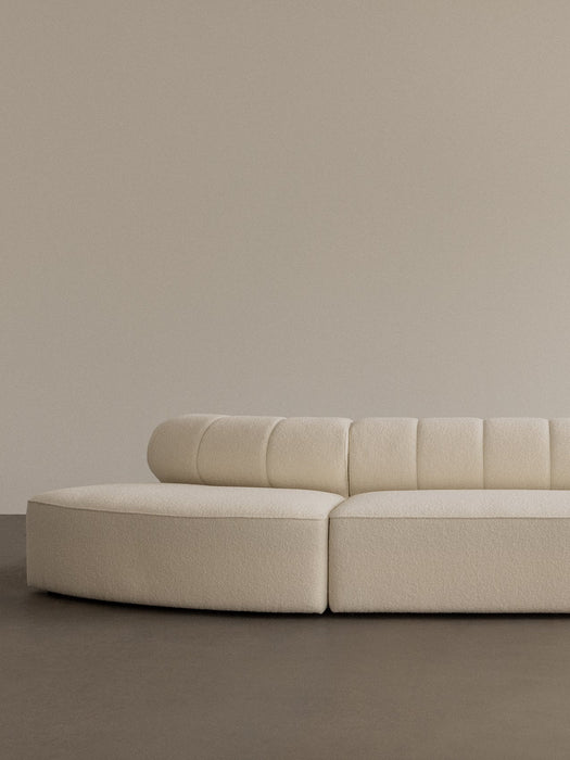 A close-up of the Eave Seamline Modular Sofa in cream bouclé, with its curved form and detailed backrest stitching.