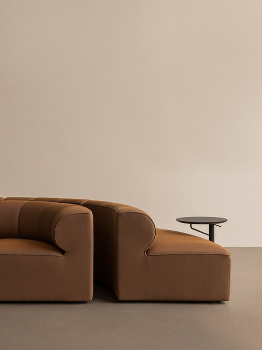 Side view of the brown Eave Seamline Modular Sofa next to a black Branch Side Table in a minimalist setting.