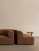 Side view of the brown Eave Seamline Modular Sofa next to a black Branch Side Table in a minimalist setting.