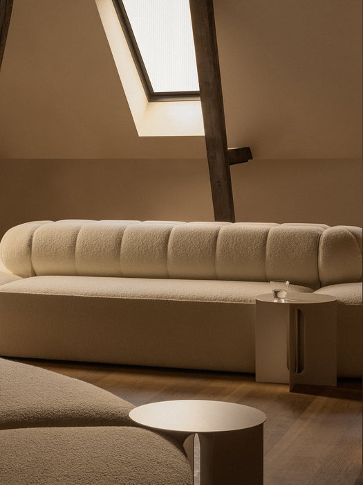 A cream Eave Seamline Modular Sofa and Androgyne Side Table on a wooden floor in a warmly lit attic room with a skylight.