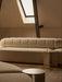 A cream Eave Seamline Modular Sofa and Androgyne Side Table on a wooden floor in a warmly lit attic room with a skylight.