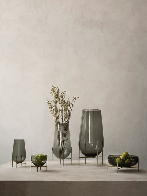 The Echasse Series by Theresa Rand for Audo: smoked glass vases and bowls on brass stands, styled with fruit and botanicals.